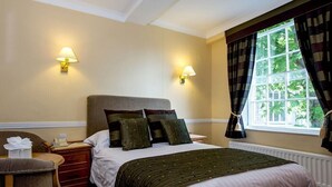 A hotel room with a bed, bedside lamps, a chair, a small table, and a window with curtains. - Prince Rupert Hotel (Shrewsbury)