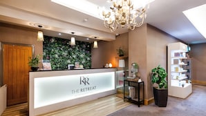 A reception desk with a sign reading "The Retreat at Redworth Hall," a chandelier, a wall with a green leafy design, and a small plant on a table. - Redworth Hall Hotel (Newton Aycliffe)
