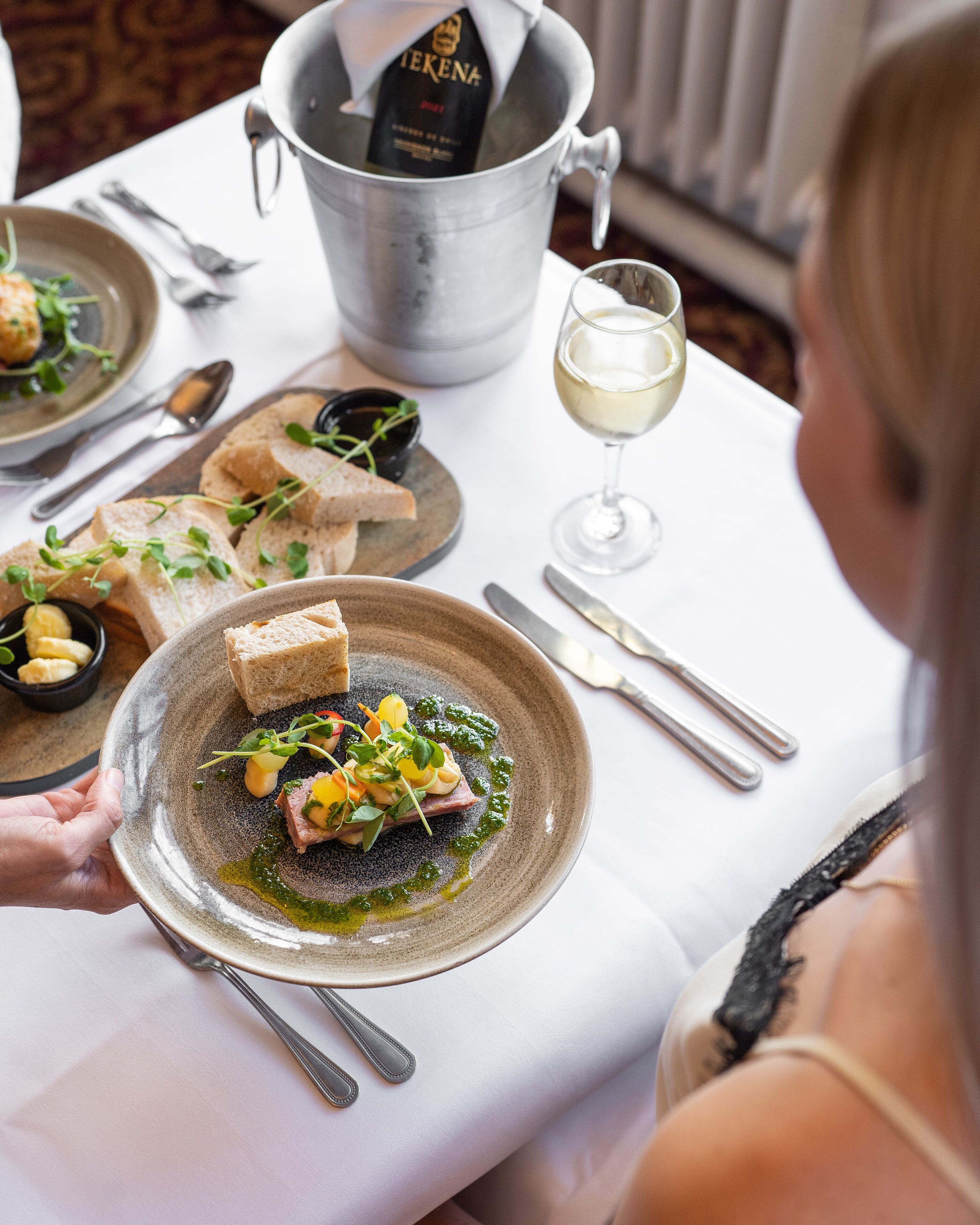 A dining table with a plate of food, a wine glass, and a bottle of champagne.