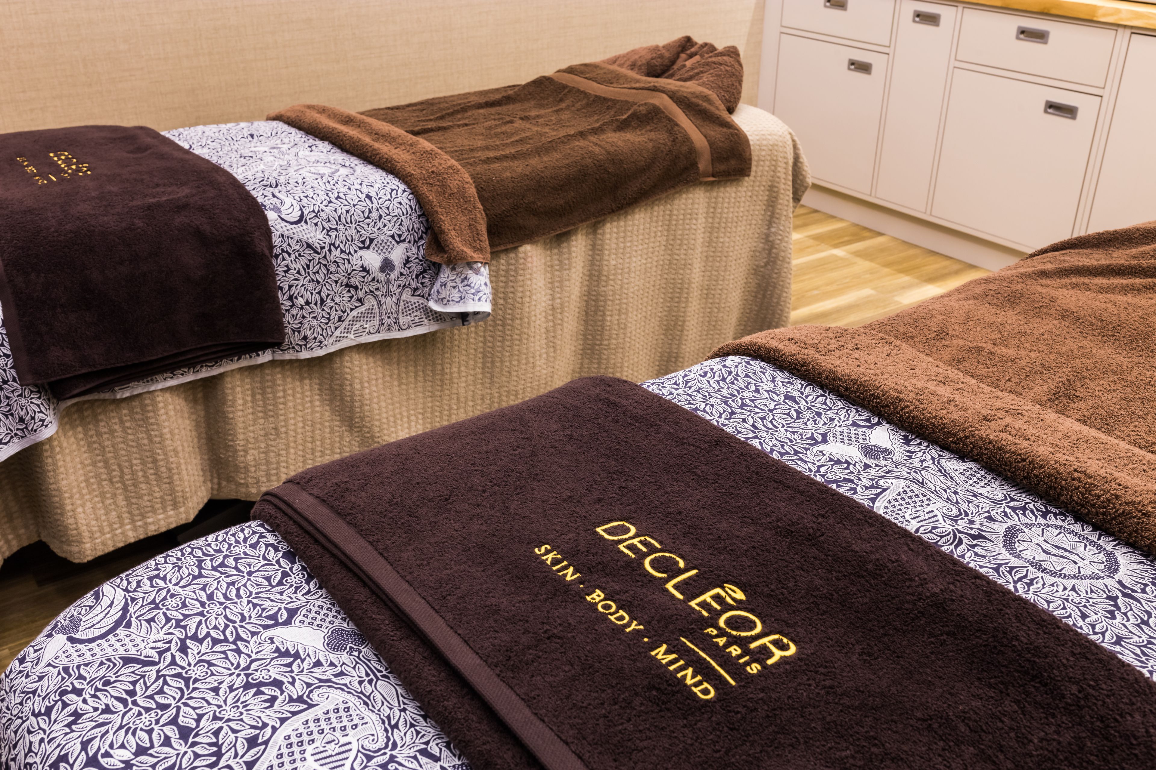 A massage room with two massage tables covered with patterned towels and a brown blanket.