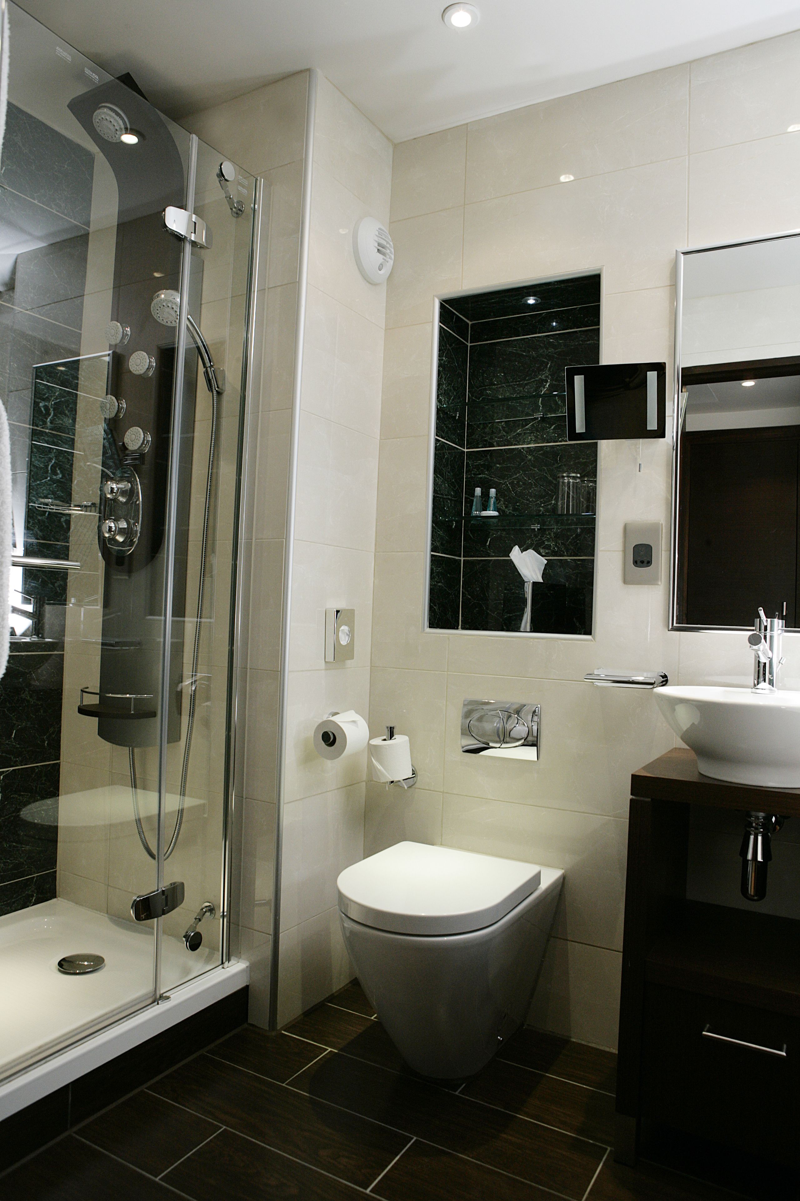 A modern bathroom with a glass-enclosed shower, a white toilet, and a dark wooden vanity with a mirror.