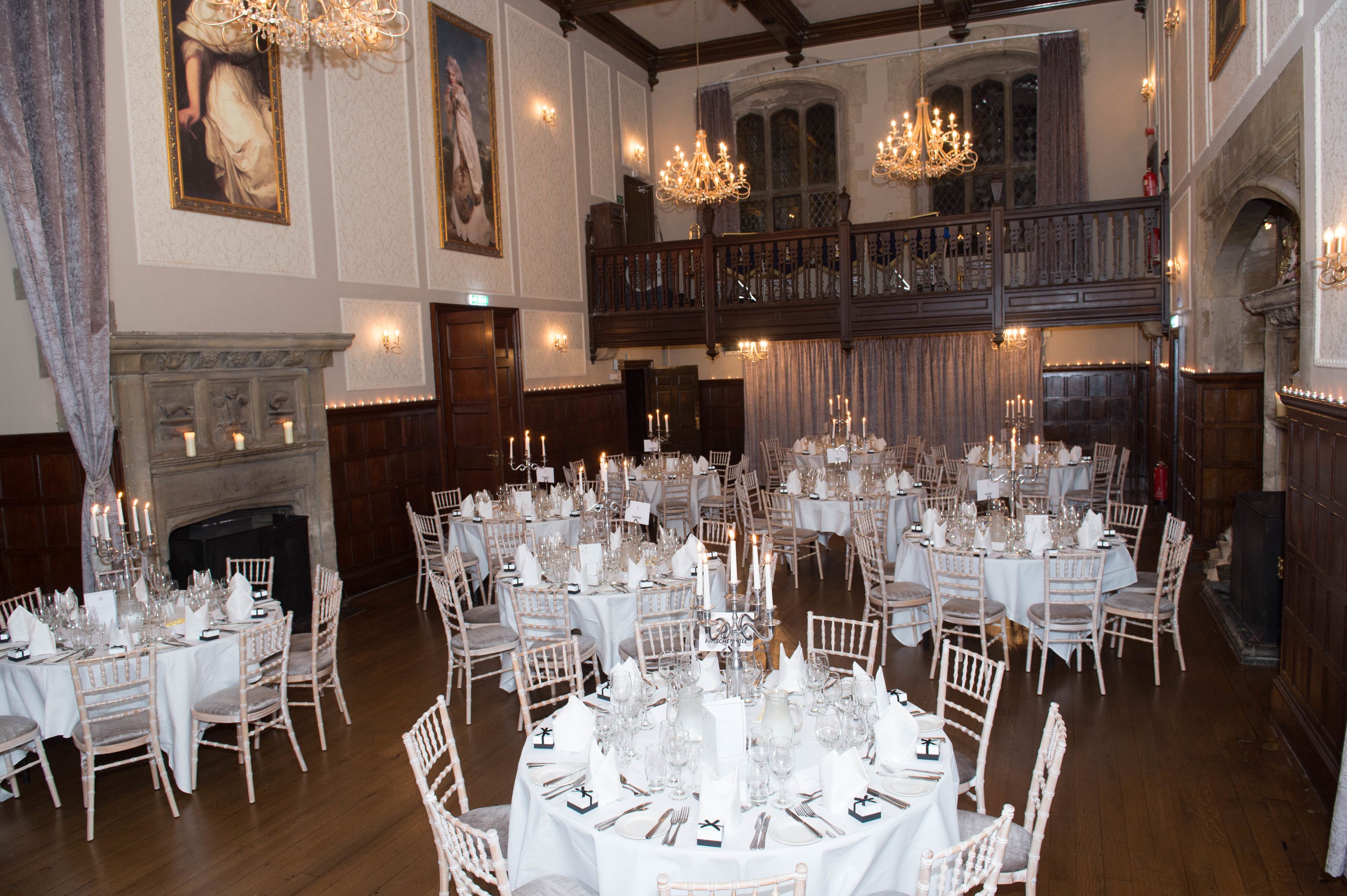 A grand banquet hall with multiple round tables set for a formal event, featuring chandeliers and classical architecture.