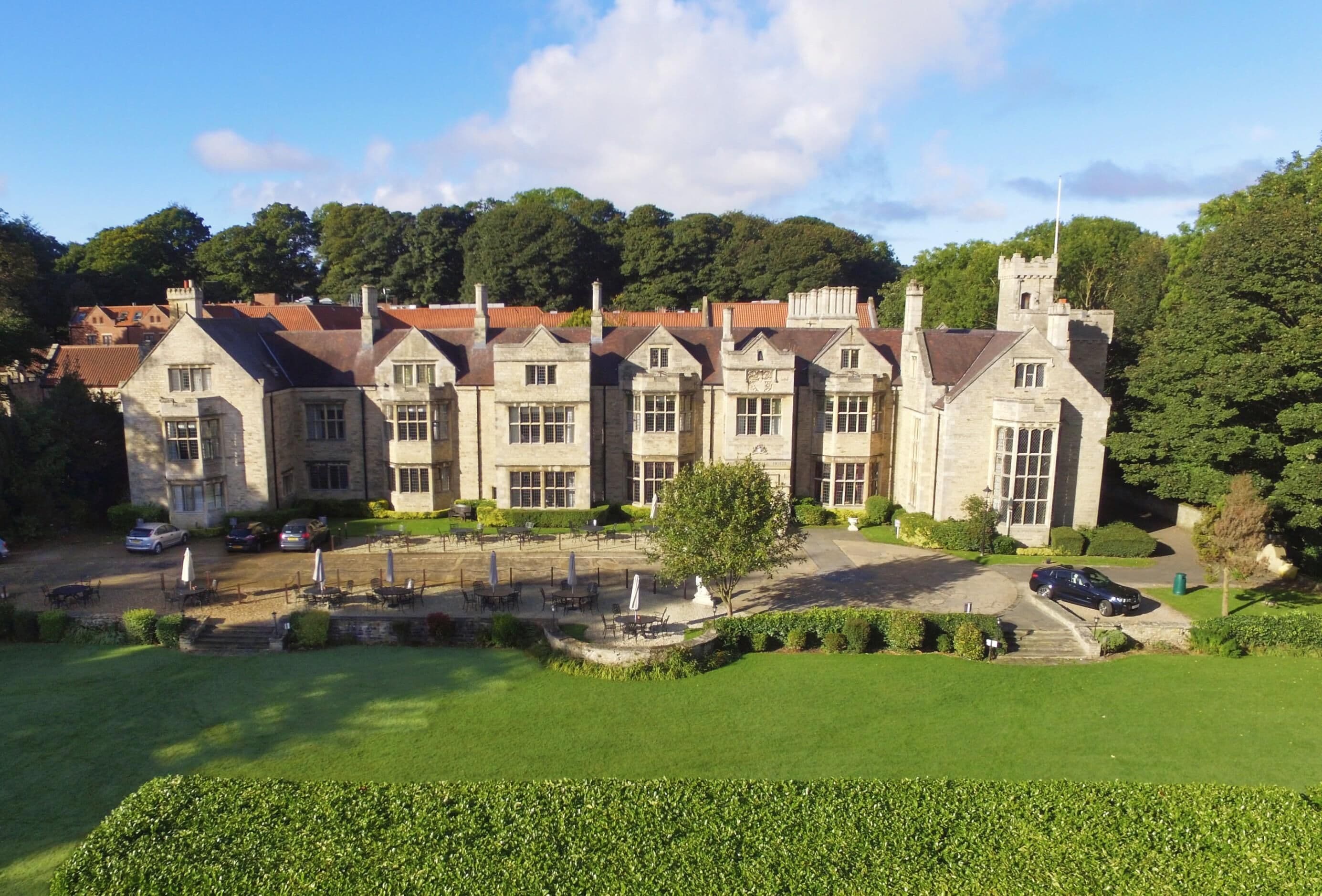 A large stone building with multiple windows and a central tower, surrounded by a well-maintained lawn and outdoor seating area.