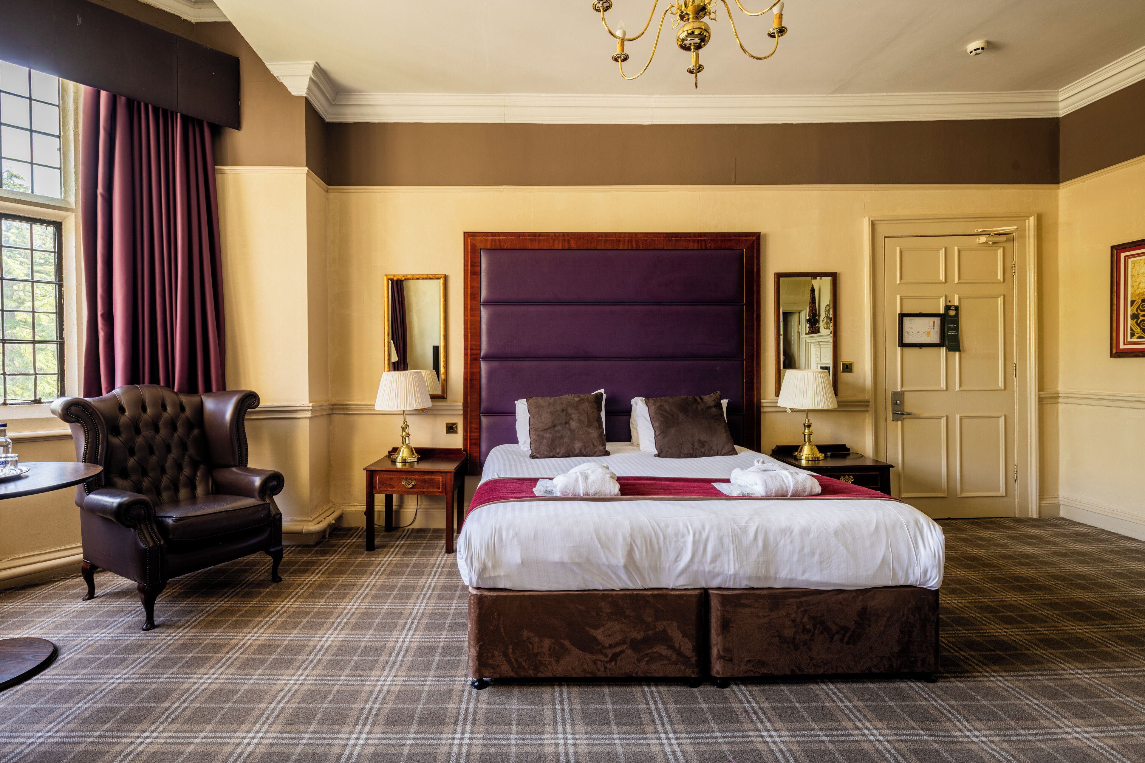 A hotel room with a large bed, a chair, a nightstand, a lamp, a mirror, and a door.