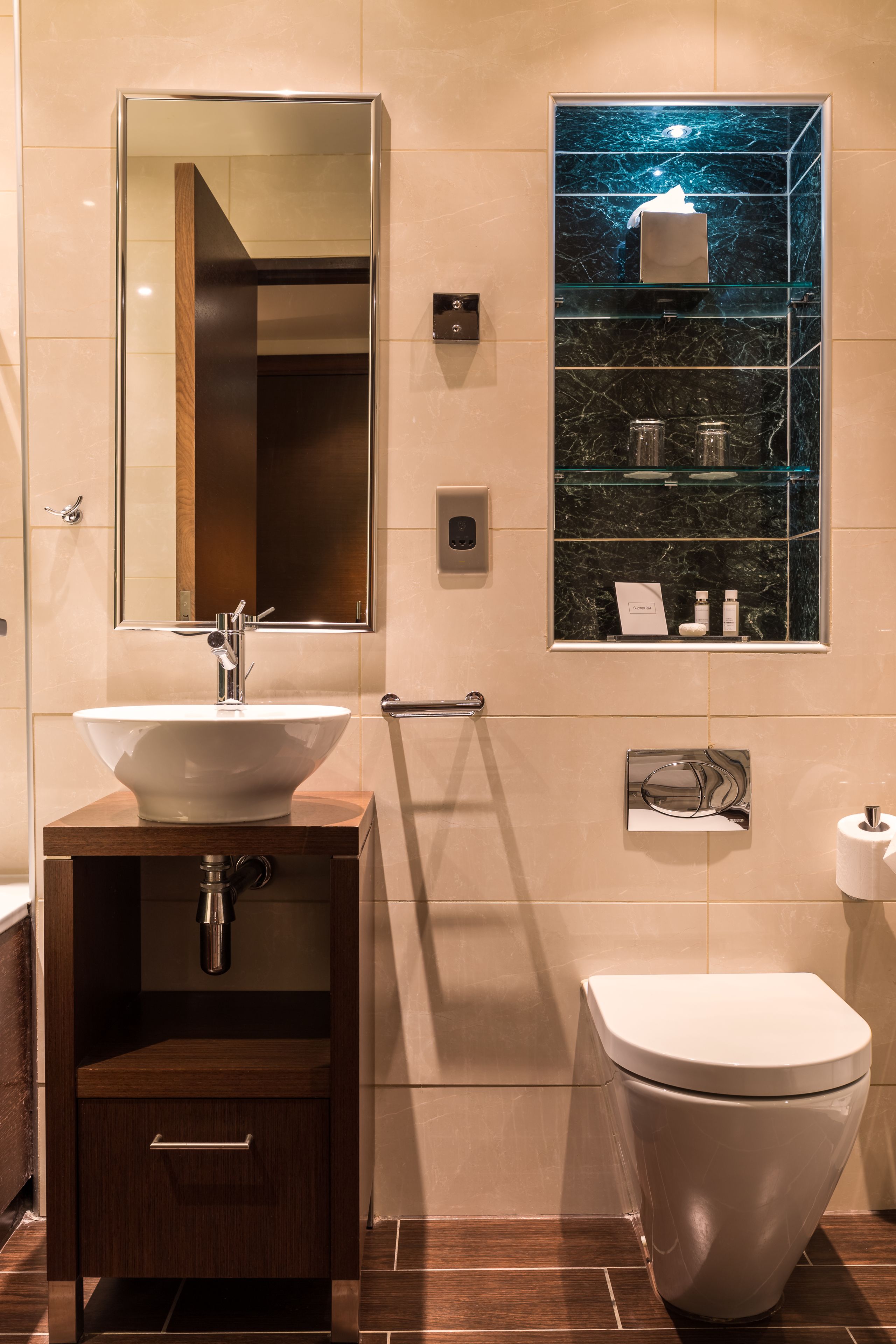 A modern bathroom with a large mirror, a sink, a toilet, and a glass-enclosed shelf with toiletries.