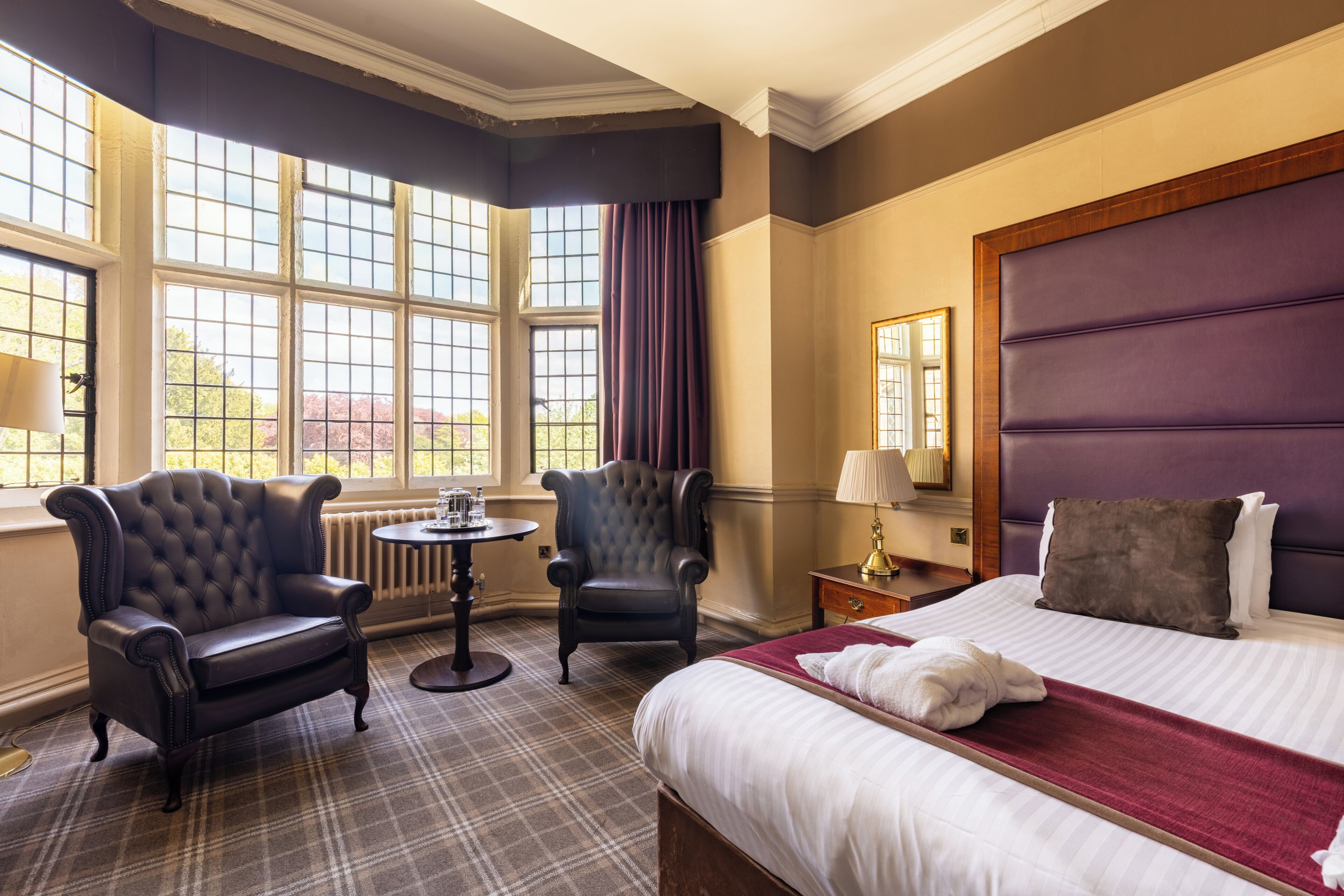 A hotel room with a large bed, two armchairs, a small table, and a window with curtains.