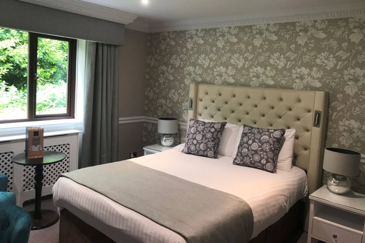 Ein ordentlich eingerichtetes Schlafzimmer mit einem großen Bett, einem kleinen runden Tisch und einem Fenster mit Vorhängen.
