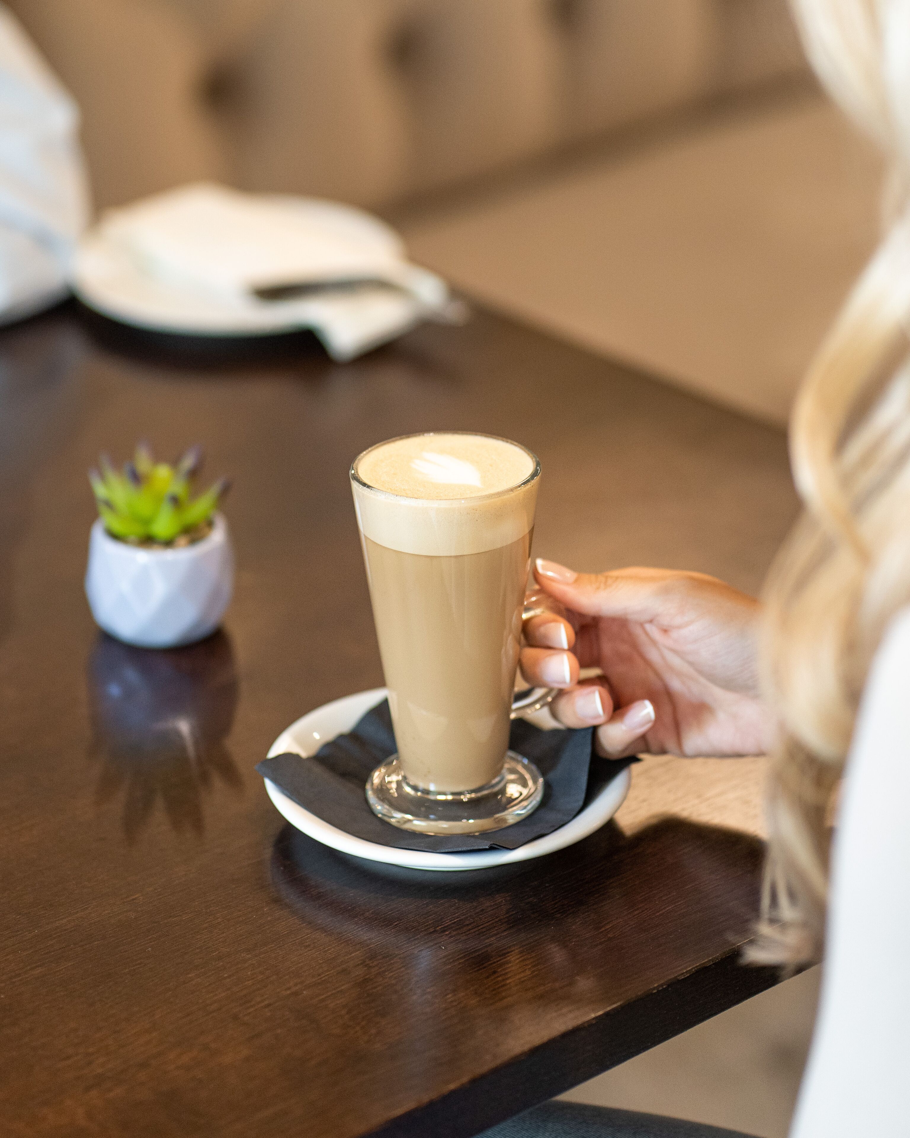 A cup of coffee on a saucer with a small plant beside it.