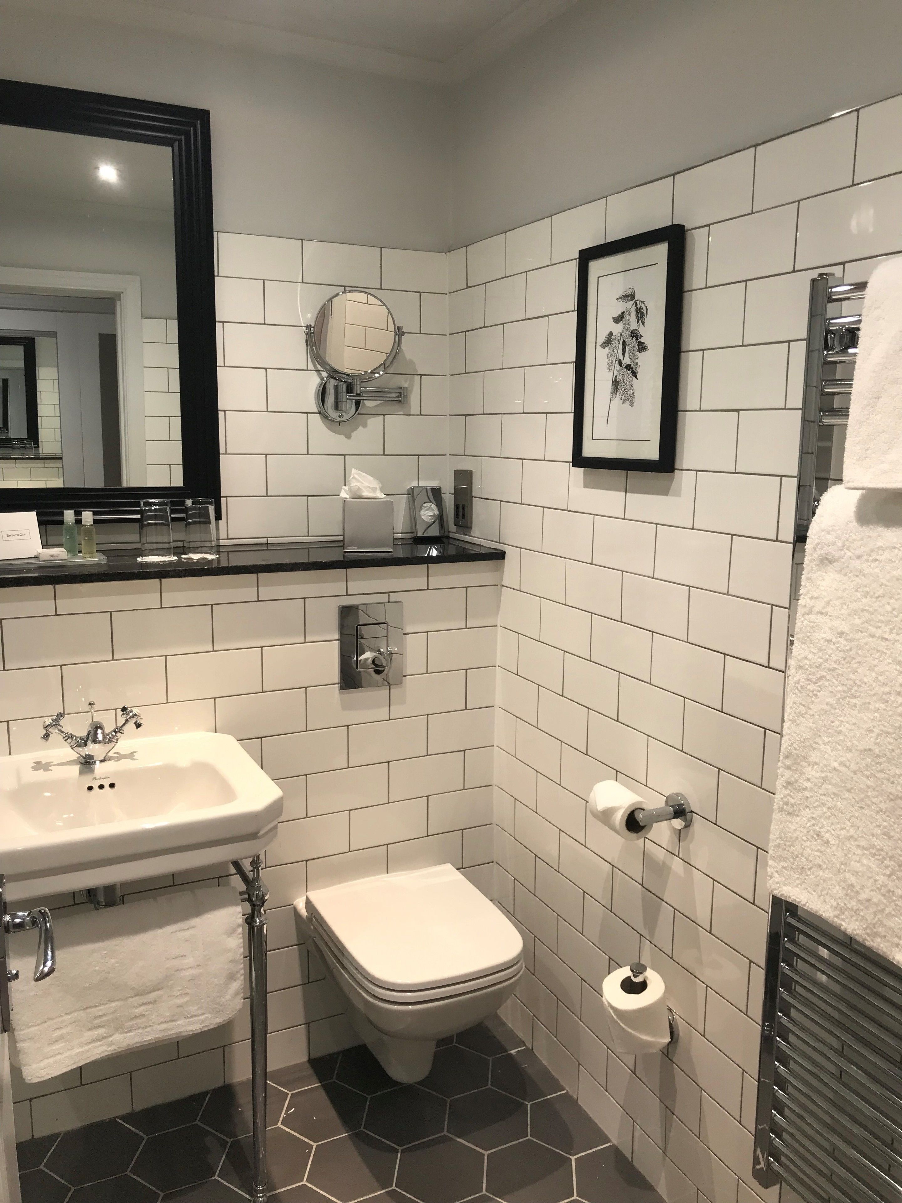 A modern bathroom with white tiles, a sink, a toilet, a framed picture, and a towel rack.