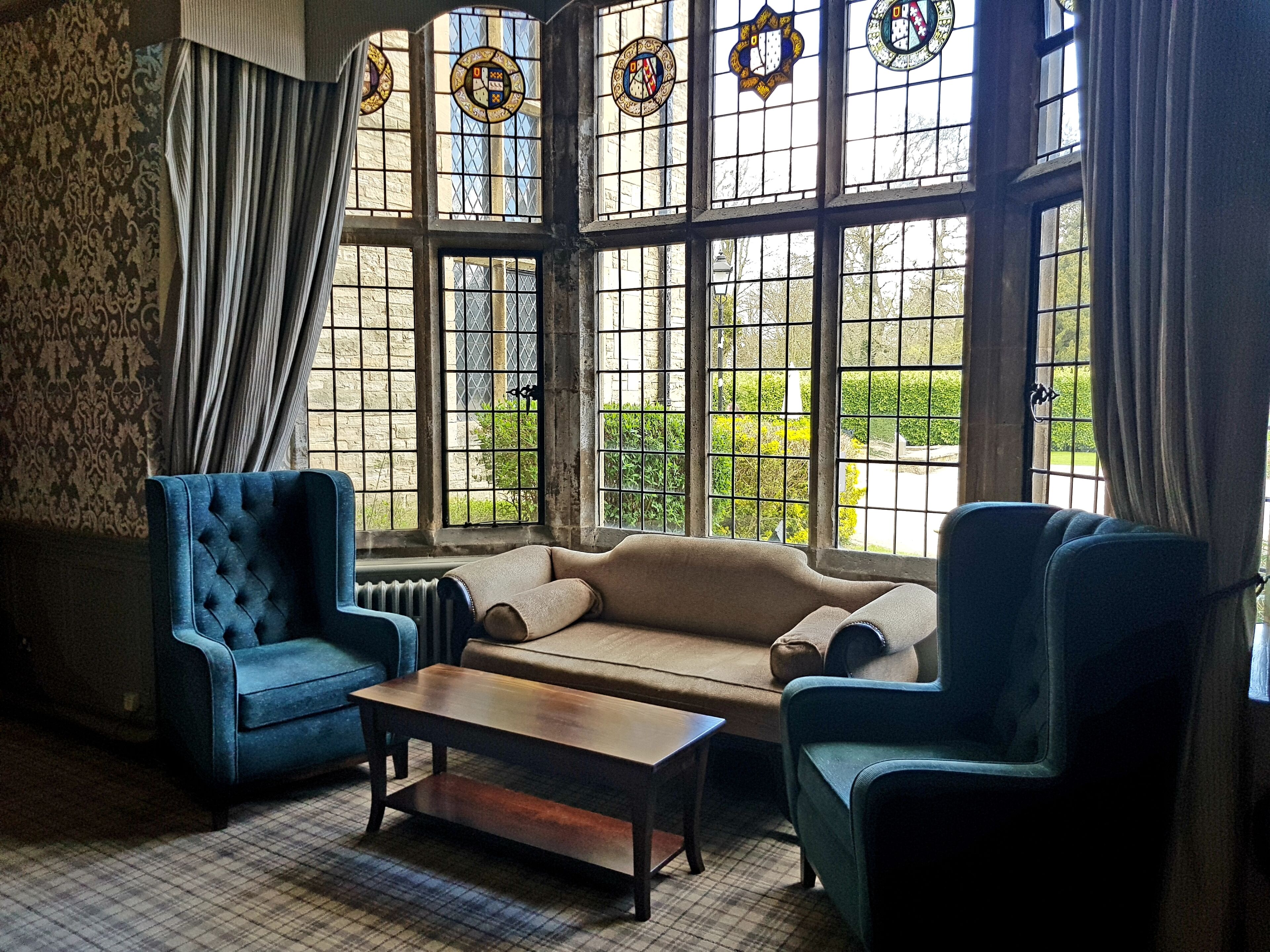 A room with a sofa, two armchairs, a coffee table, and large windows with stained glass.