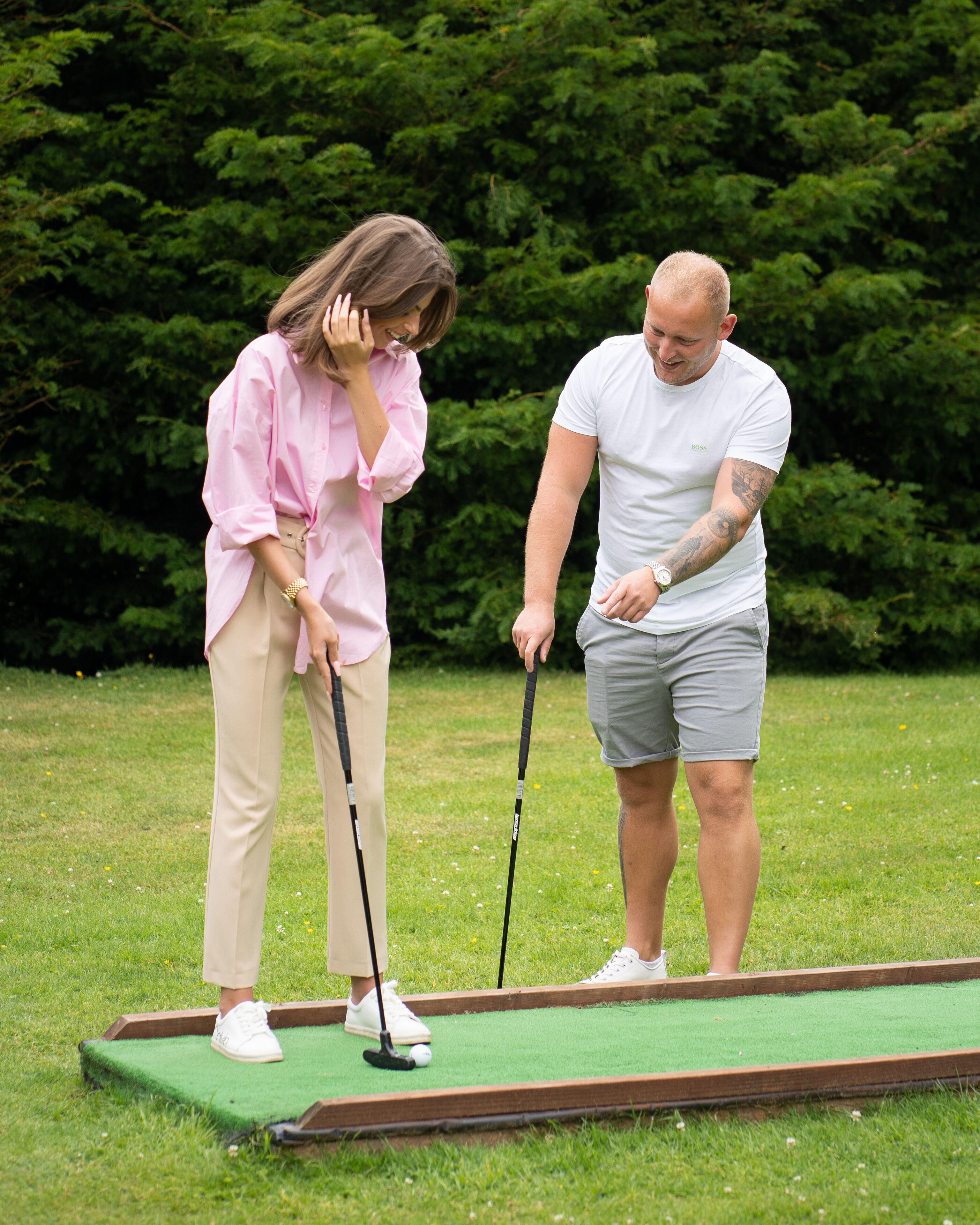 Two people playing golf on a green field with trees in the background.