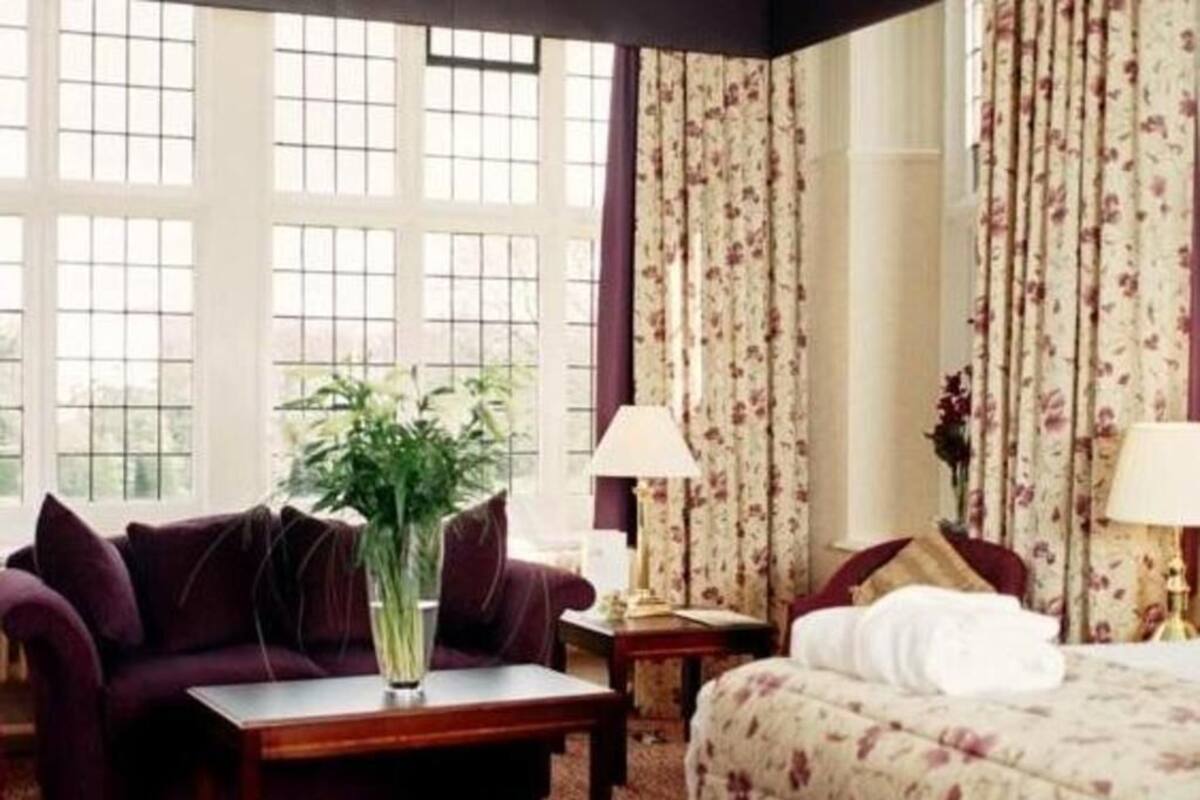 Ein Hotelzimmer mit großem Fenster, einer Couch, einem Bett, einem Nachttisch und einer Lampe.