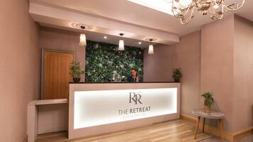 A reception area with a modern design, featuring a reception desk, a wooden door, and a decorative wall with plants.