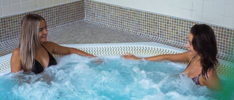 Two women in a hot tub with tiled walls and a tiled floor.