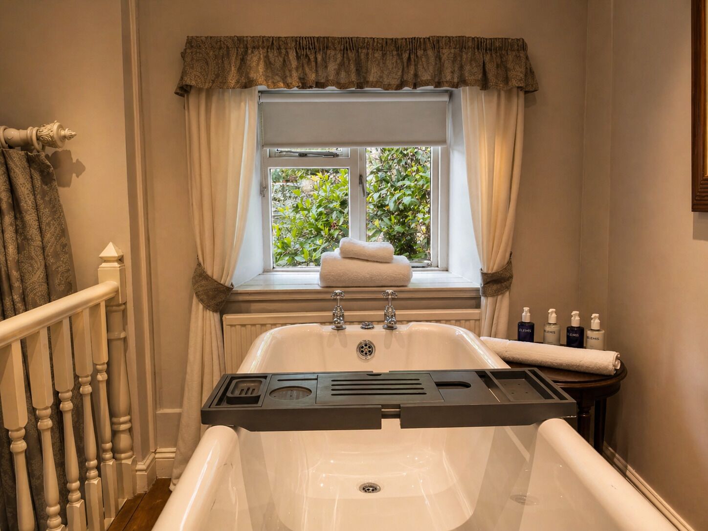 A bathroom with a bathtub, window with curtains, and a towel rack.