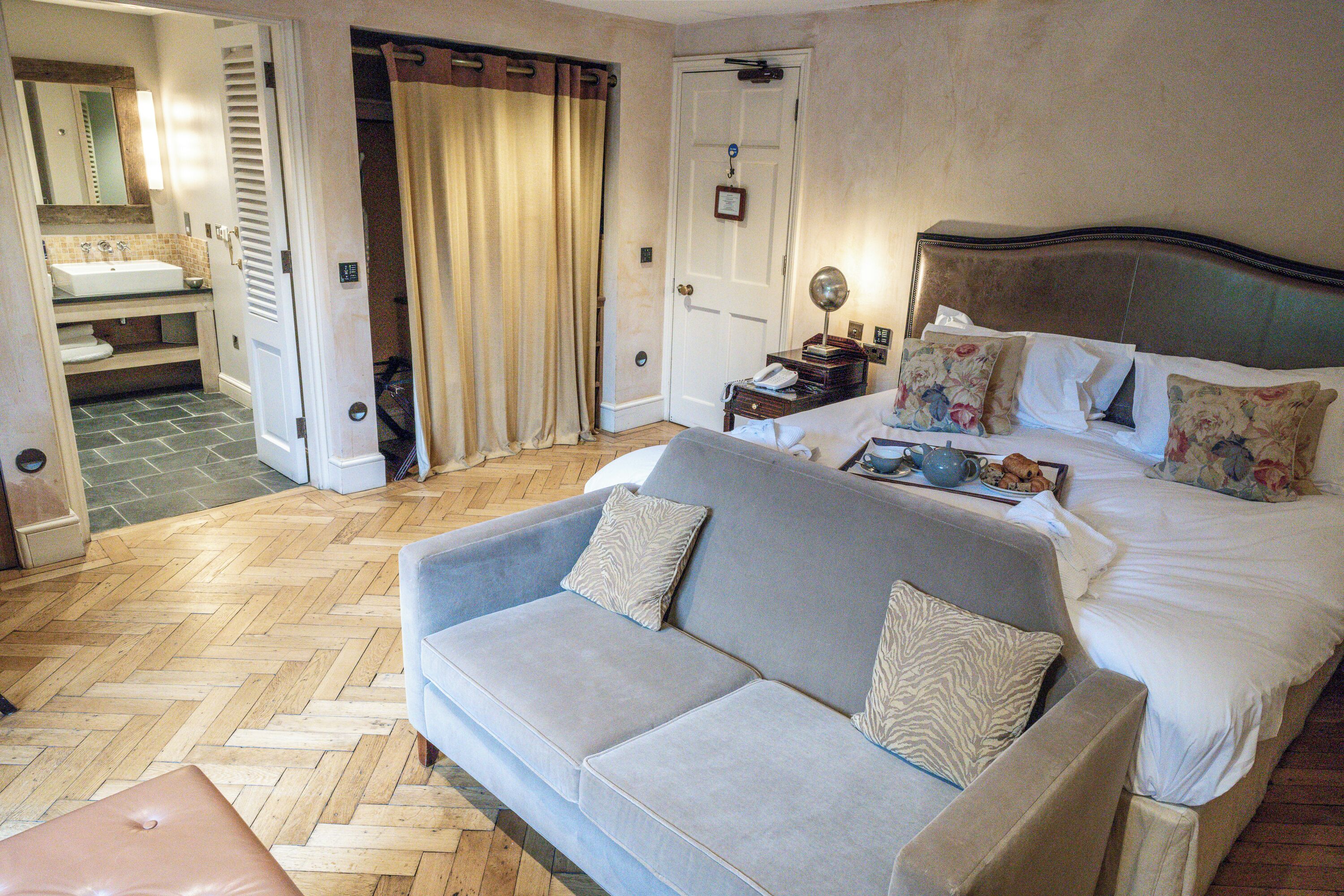A hotel room with a bed, a sofa, a bathroom with a sink and toilet, and a herringbone-patterned floor.