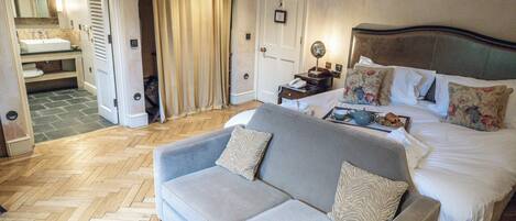 Habitación de hotel con cama, sofá, baño con lavamanos e inodoro, y piso con estampado de espiga.