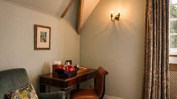 A room with a wooden ceiling, a desk with a fruit bowl, a leather chair, a cushioned armchair, a framed picture, and a window with curtains.