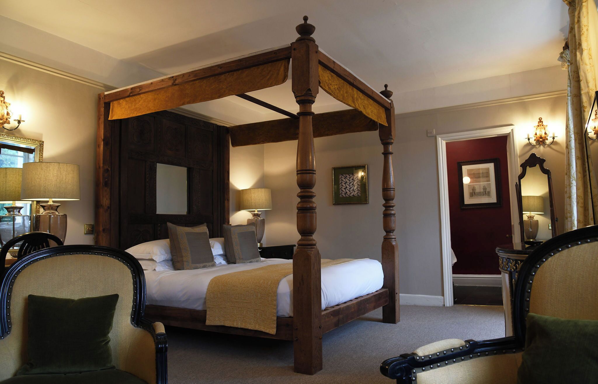 A four-poster bed in a room with a mirror, two lamps, and a door with a picture.