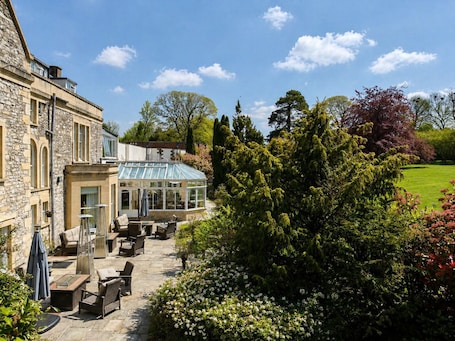 A stone building with a conservatory, outdoor seating, and a well-maintained garden.