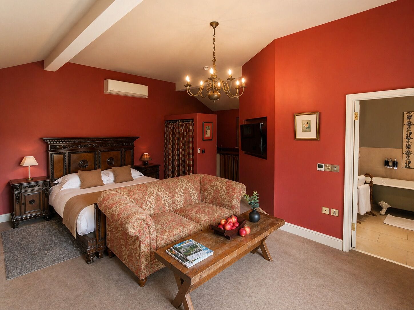 A bedroom with a bed, a sofa, a coffee table with magazines, a chandelier, and a TV.