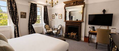 Een hotelkamer met een groot bed, een open haard, een televisie en twee fauteuils.