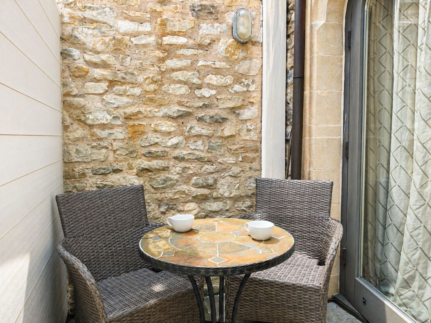 A corner with two wicker chairs and a round table with a mosaic top.