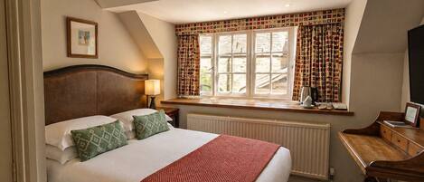 A bedroom with a bed, a desk, a radiator, a window with curtains, and a picture on the wall.