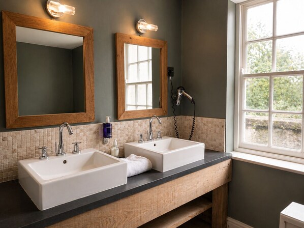 A bathroom with two sinks, a large mirror, and a window with a view of greenery.
