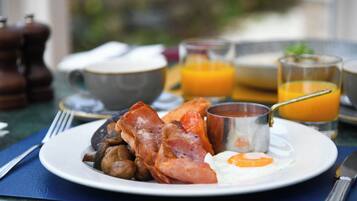 A breakfast plate with bacon, mushrooms, and a fried egg. There are glasses of orange juice and a coffee cup in the background.