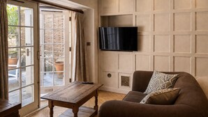 A living room with a flat-screen TV mounted on a wall, a brown sofa with patterned cushions, a wooden coffee table, and a sliding glass door leading to an outdoor area. - Montigo Resorts, Somerset (Shepton Mallet)