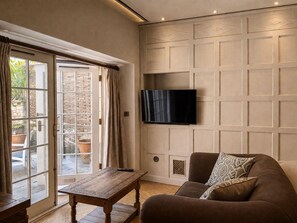 A living room with a flat-screen TV mounted on a wall, a brown sofa with patterned cushions, a wooden coffee table, and a sliding glass door leading to an outdoor area. - Montigo Resorts, Somerset (Shepton Mallet)