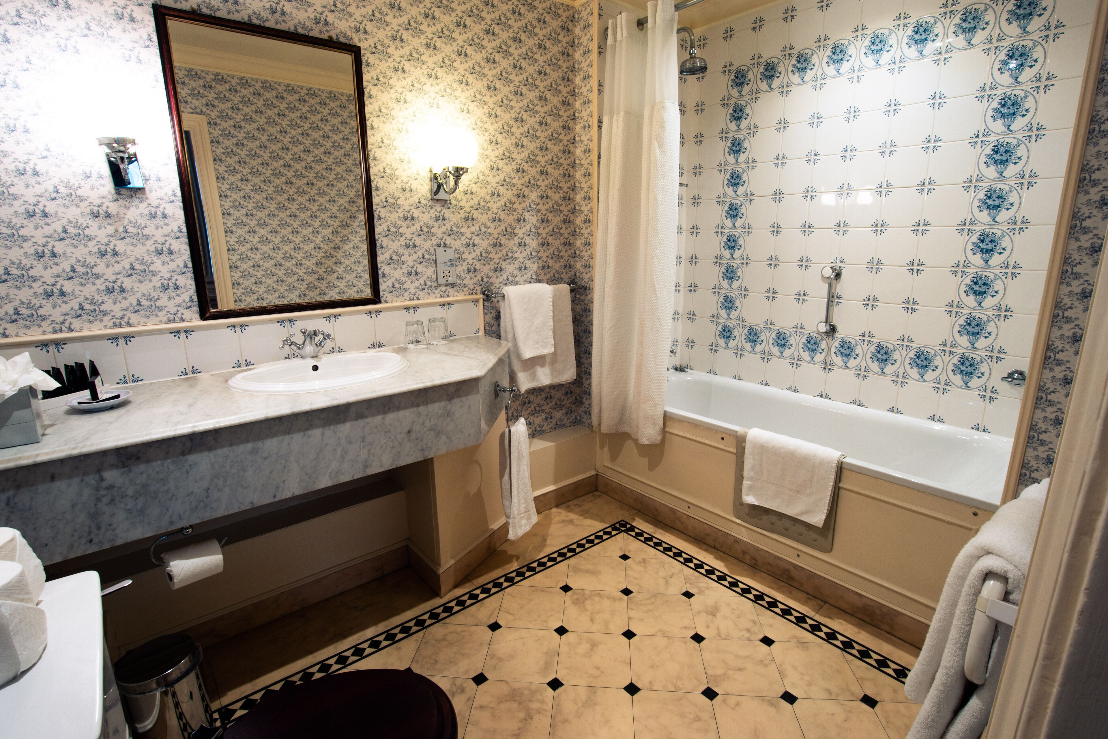 A bathroom with a double sink, a bathtub, a mirror, and patterned tiles.
