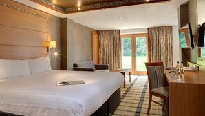 Habitación de hotel con una cama grande, un escritorio con silla, televisor y vista al exterior.