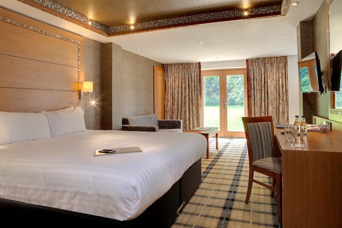 Een hotelkamer met een groot bed, een bureau met stoel, een televisie en uitzicht op het landschap.