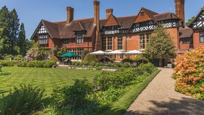 Un edificio grande y antiguo con múltiples chimeneas y arquitectura de estilo Tudor, rodeado de jardines cuidados y zonas de estar al aire libre.