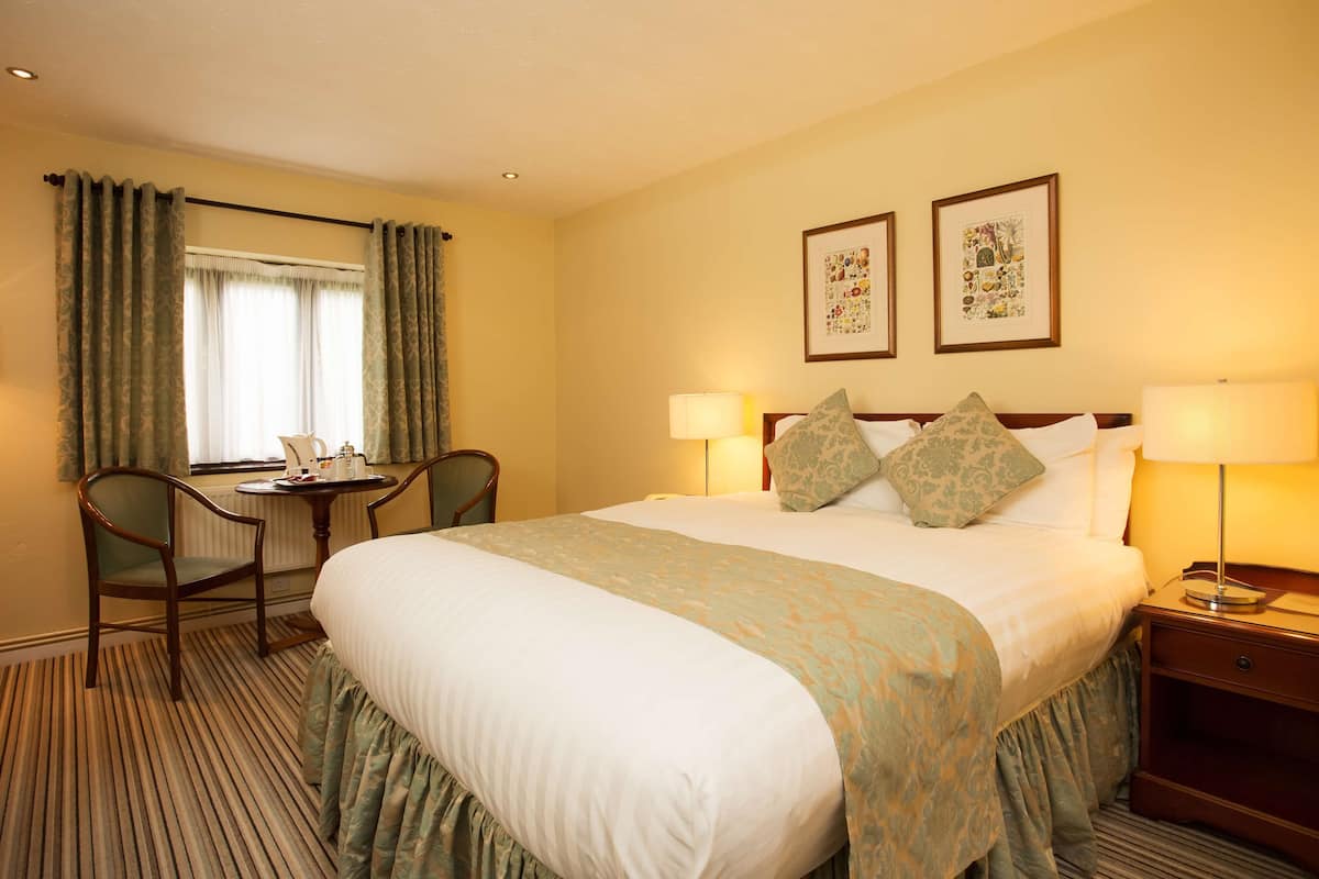 Een hotelkamer met een groot bed, twee bedlampen, een bureau met stoel, en twee afbeeldingen in lijsten aan de muur.