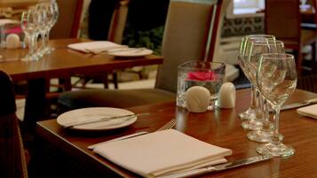 Comedor con mesas dispuestas para dos, cada una con copas de vino, platos y cubiertos.