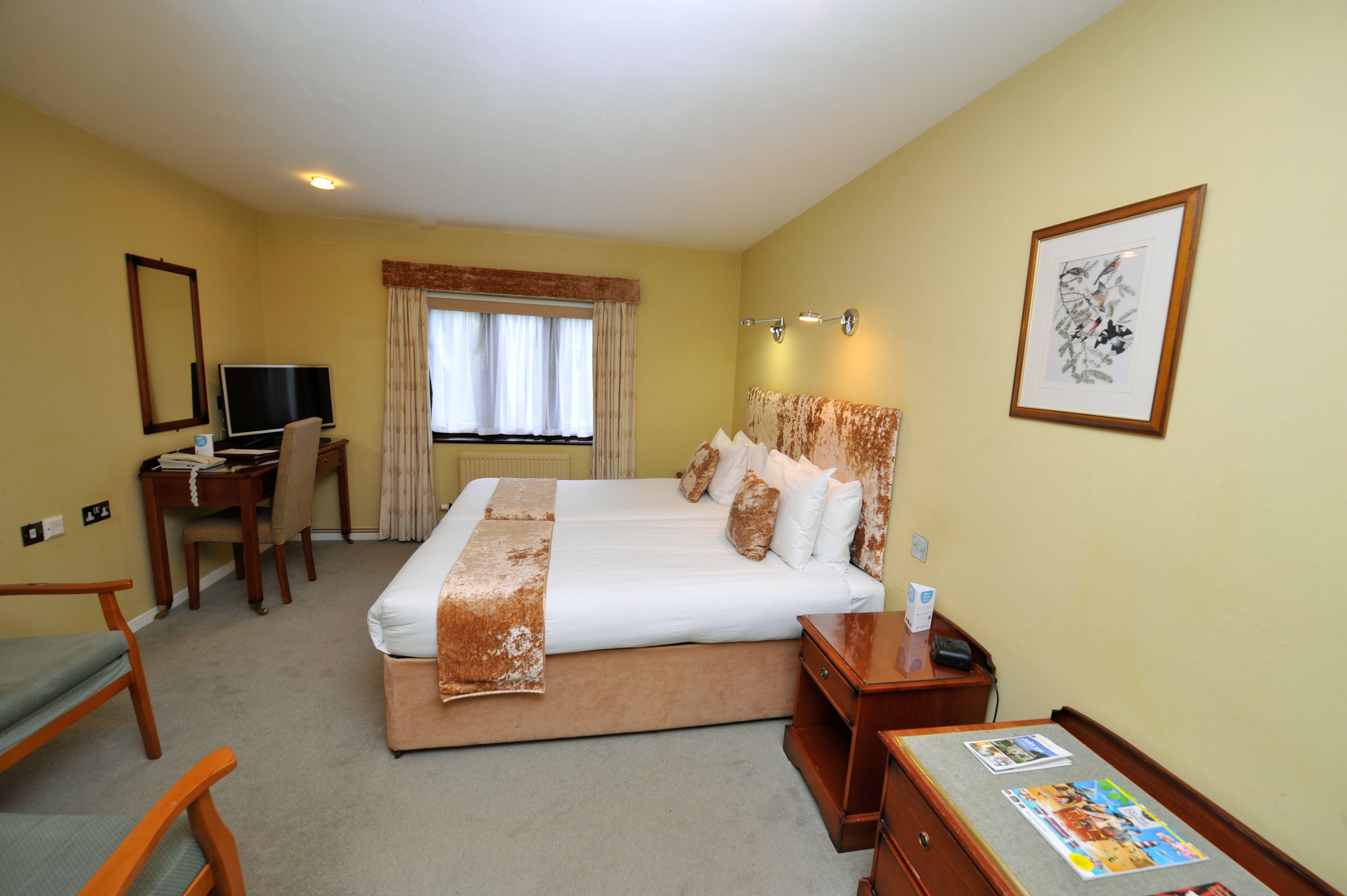 A hotel room with a large bed, a desk with a computer, a chair, and a small table with magazines.
