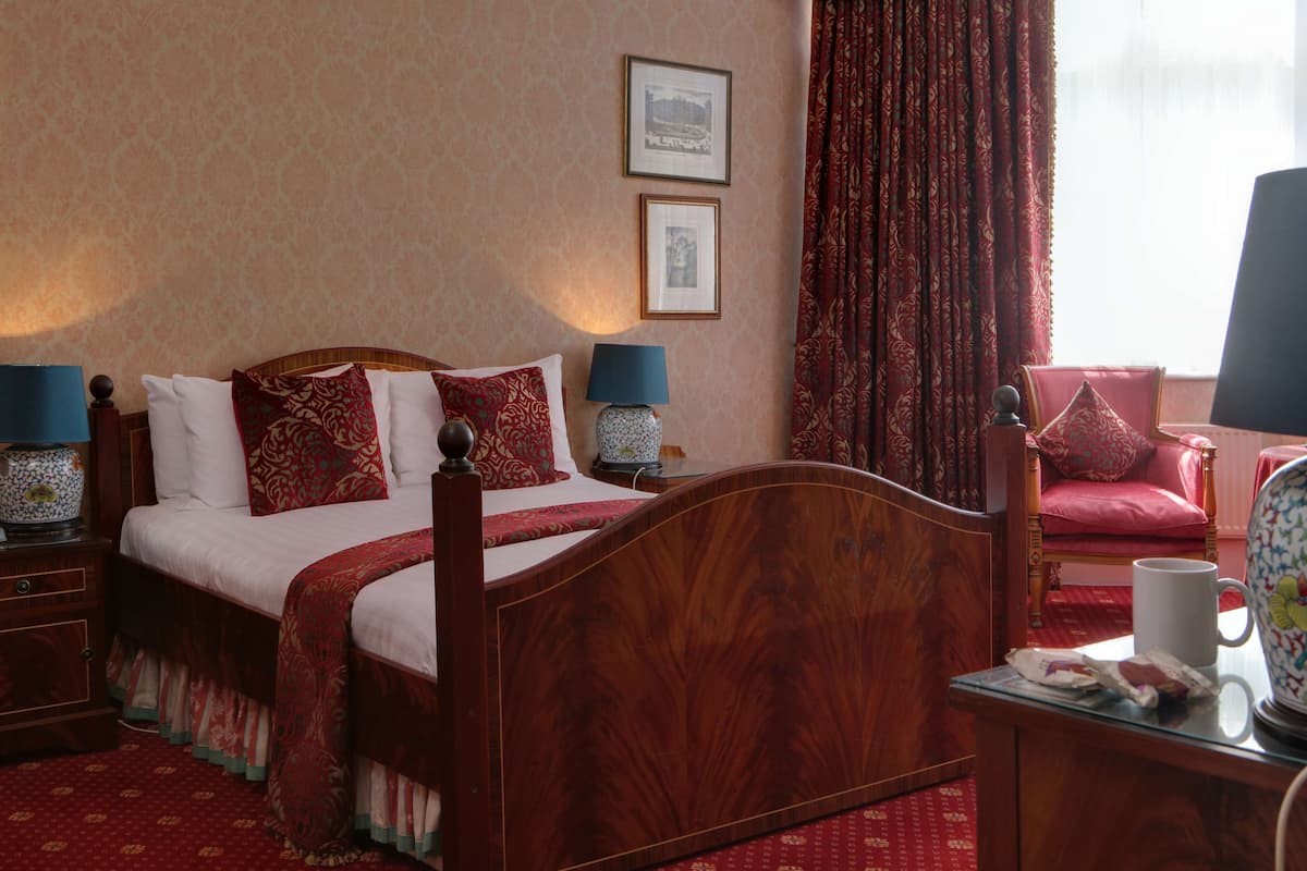 Een traditionele slaapkamer met een houten bed, twee nachtkastjes, een rode stoel en een raam met rode gordijnen.