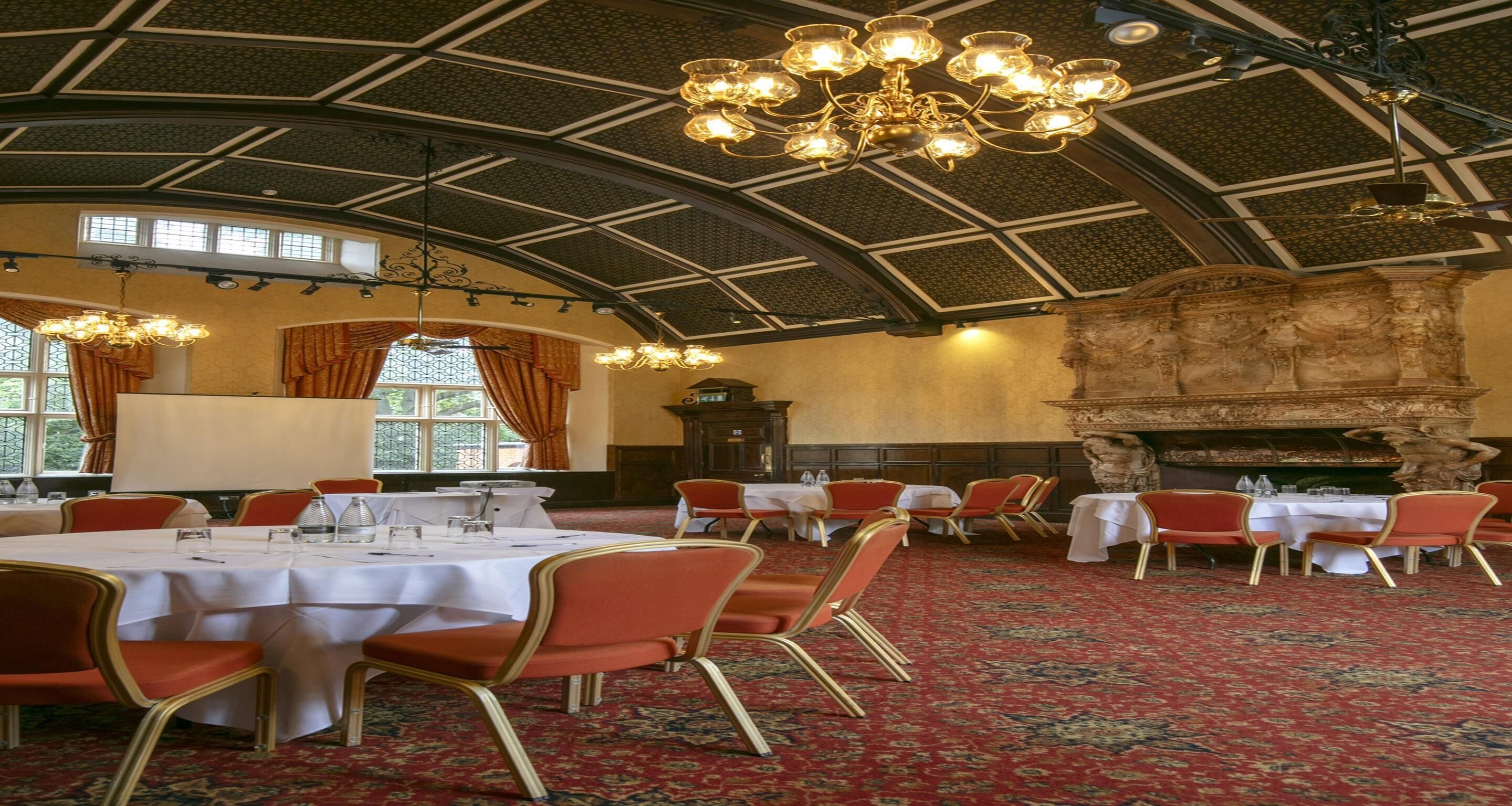 Ein Festsaal mit runden Tischen, rot gepolsterten Stühlen und einer großen Kristallleuchtre.