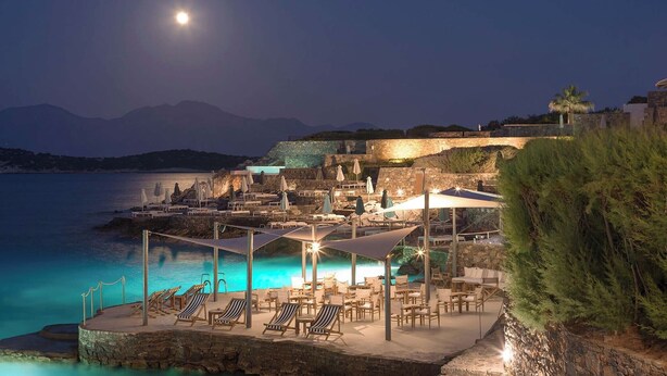 Un resort costero con terraza al aire libre, piscina y vistas al mar y a las montañas.
