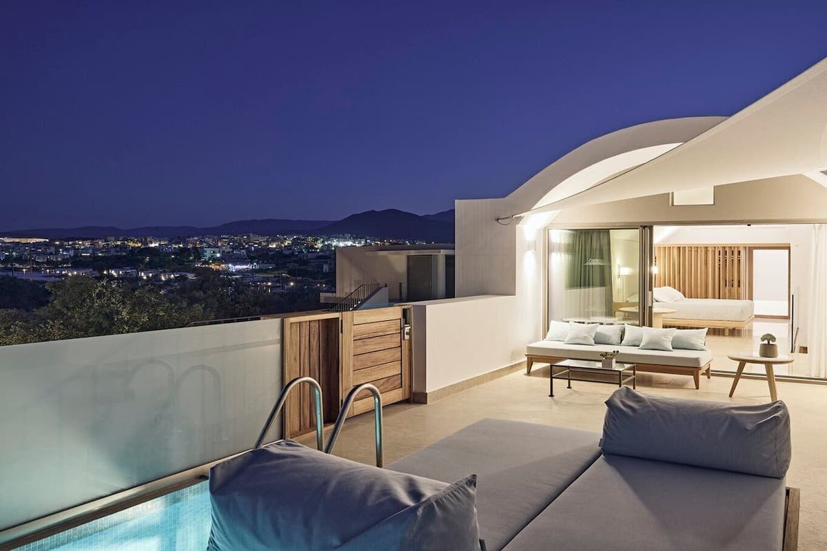 A modern rooftop terrace with a pool, seating area, and a view of the city at night.