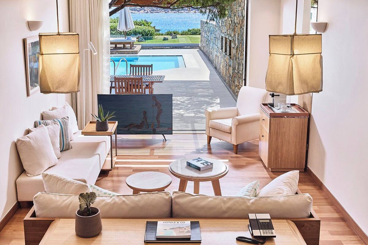 A modern hotel room with a sofa, armchairs, a coffee table, and a view of a swimming pool and outdoor area.