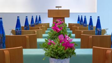 Un salón de conferencias con sillas de madera, una mesa verde y un arreglo floral central.
