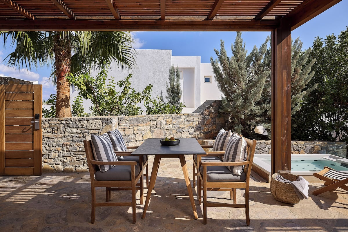An outdoor patio with a table and chairs, a stone wall, a wooden pergola, and a pool.
