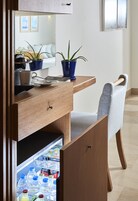 A compact hotel room with a wooden desk, a chair, a mirror, and a mini-fridge stocked with beverages.