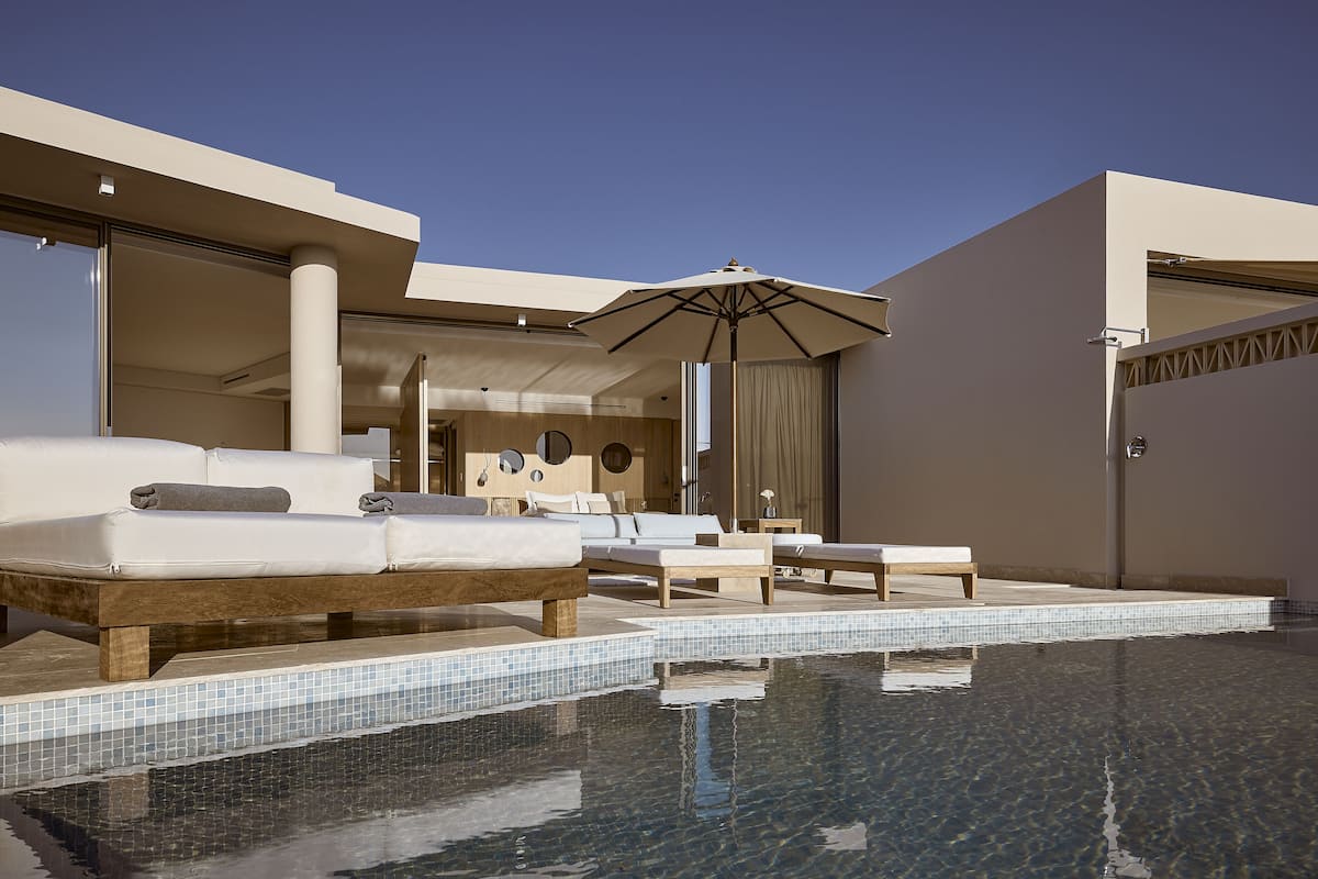 A modern outdoor pool area with lounge chairs and a large umbrella, surrounded by a minimalist architectural design.