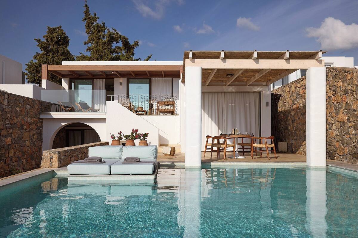 A modern poolside area with a lounge chair, a dining table, and a covered seating area.