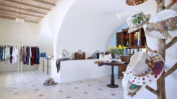 A boutique hotel interior with a white arched ceiling, a clothing rack, a table with hats, and a display of shoes.